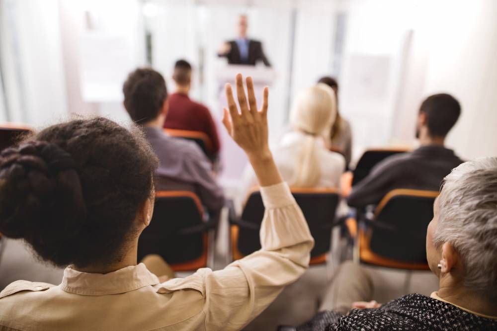 Rear view of a woman raising her hand to ask a question at a conference session.