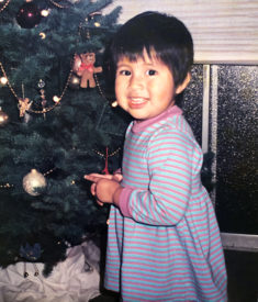 Gemma as a toddler standing next to a Christmas tree