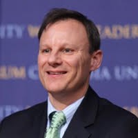 A man smiling wearing a dark suit and a green tie