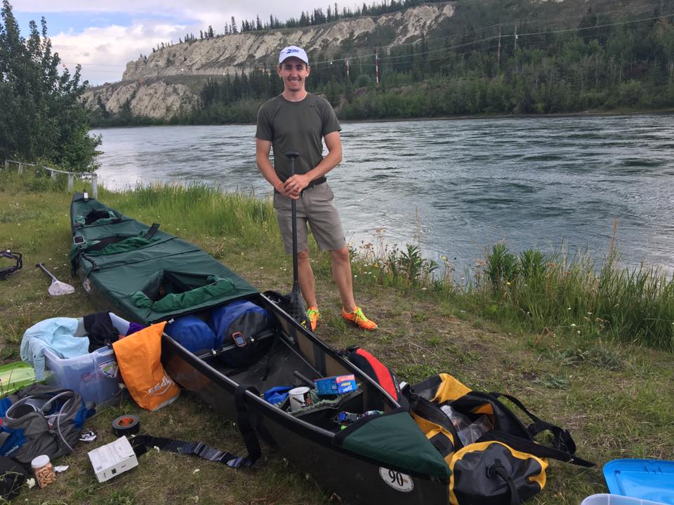 man standing next to canoe near river