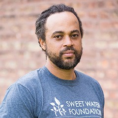 Alumnus Emmanuel Pratt is also a recipient of a 2019 'genius" grant. Man with beard and blue-gray T-shirt.