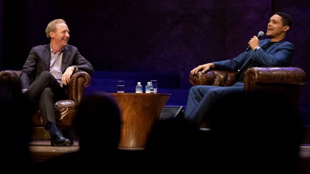 Two men sit in armchairs on a stage