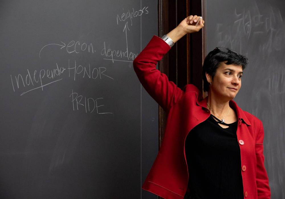 Professor stands in front of the blackboard with the words "independence," econ.," dependence," "HONOR," "PRIDE," and "neighbors" written on it