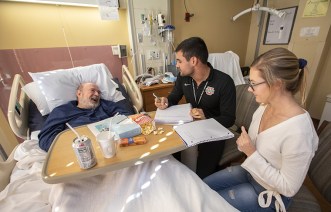 James Claspill (in bed) tells his story to WashU students, Helen Undergraduates Alex Gazo and Helen Stephens interview veteran James Claspill for "My Life, My Story." (Photo: Joe Angeles/Washington University)
