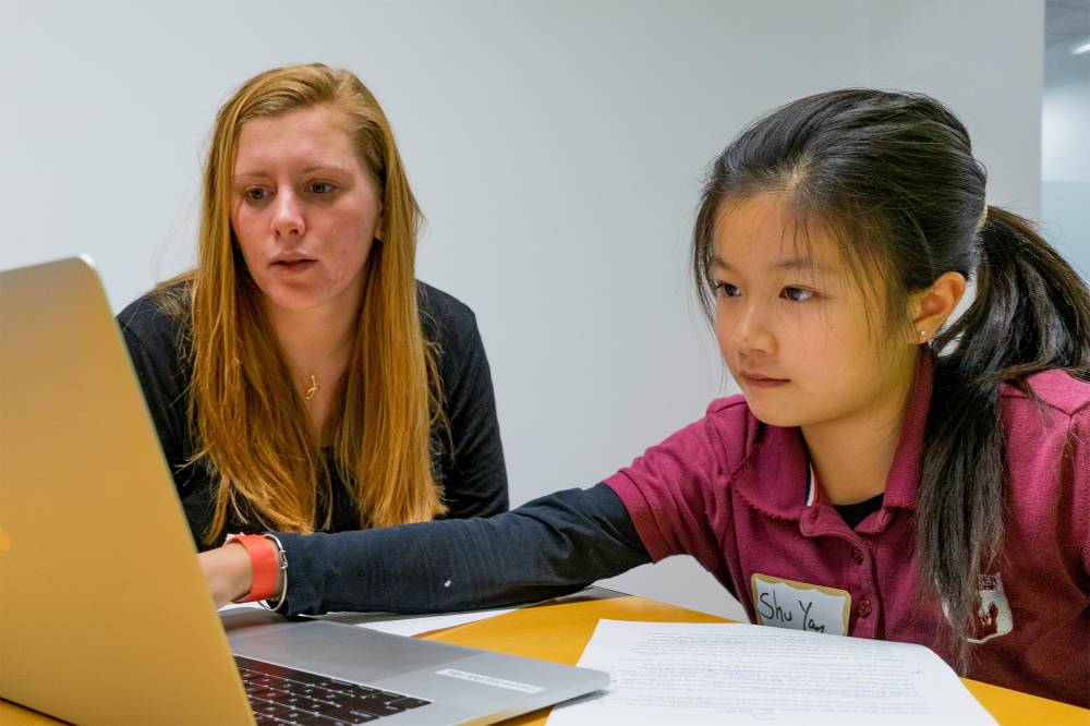 College student with mentee working on a computer.