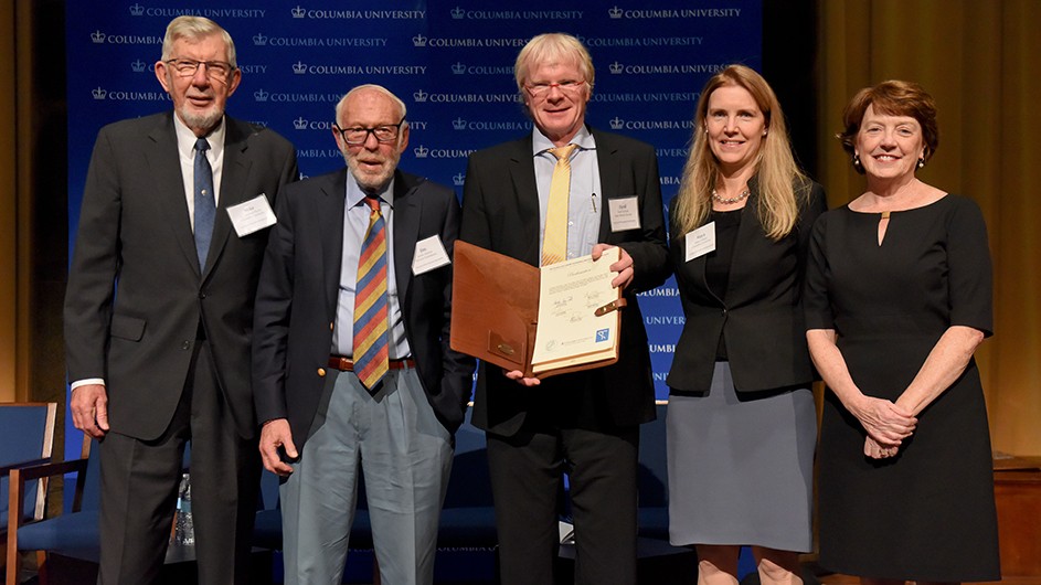 Leadership signing official document at opening event (left to right): G. Michael Purdy, Executive Vice President for Research, Columbia University; James Simons, Chairman of the Board, Simons Foundation; Ferdi Schuth, Scientific Vice-President of the Chemistry, Physics and Technology Section, Max Planck Society; Maya Tolstoy, Dean, Faculty of Arts and Sciences, Columbia University; and Mary Boyce, Dean, Fu Foundation School of Engineering and Applied Science, Columbia University. Photo: Asiya Khaki 3 men and 2 women with middle man with blonde hair, blue shirt, suite jacket yellow tie holding signed document