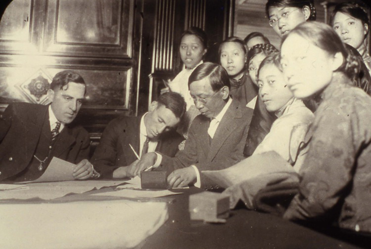 An old photo of a group of people at a table signing documents.