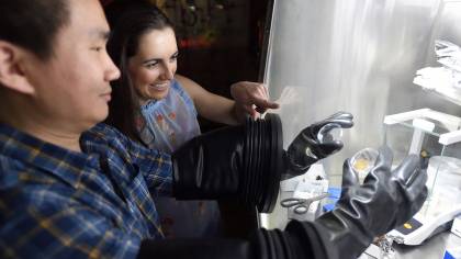 A man uses gloves in a protective box while a woman looks on