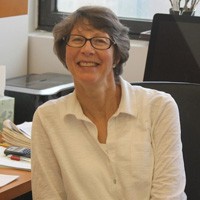 Lorraine S. Symington: A woman with short gray hair and brown oval-shaped glasses smiling, sitting in an office with window behind her. 