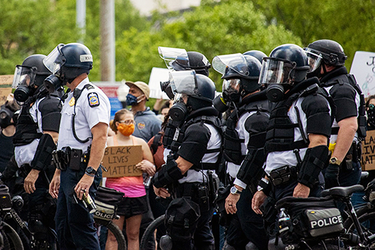 police clad in heavy riot gear march past peaceful protesters