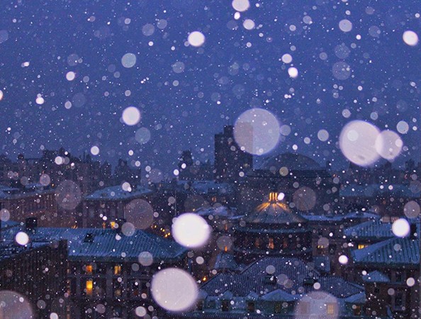 Enlarged snowflakes refract upon a blue sky background looking out over Morningside campus' domed Low library and other buildings.