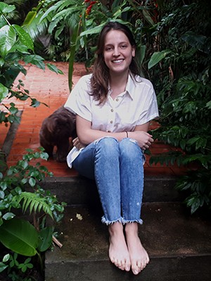 A girl wearing a white shirt and jeans sits among greenery.